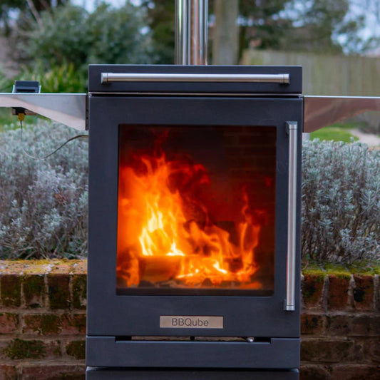 Outdoor wood stove with flames inside, surrounded by greenery