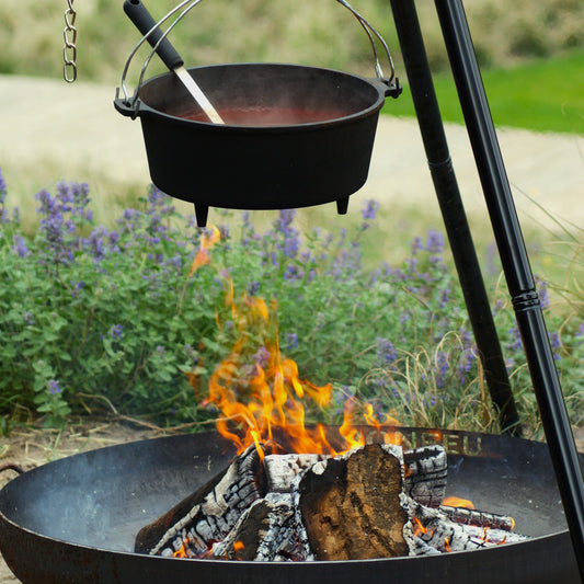 Black pot over a fire pit with flames and smoke, surrounded by greenery.
