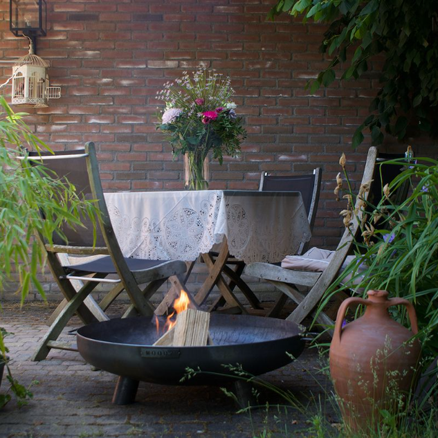 MOODZ corten steel fire bowl with feet and handles shown in a garden setting