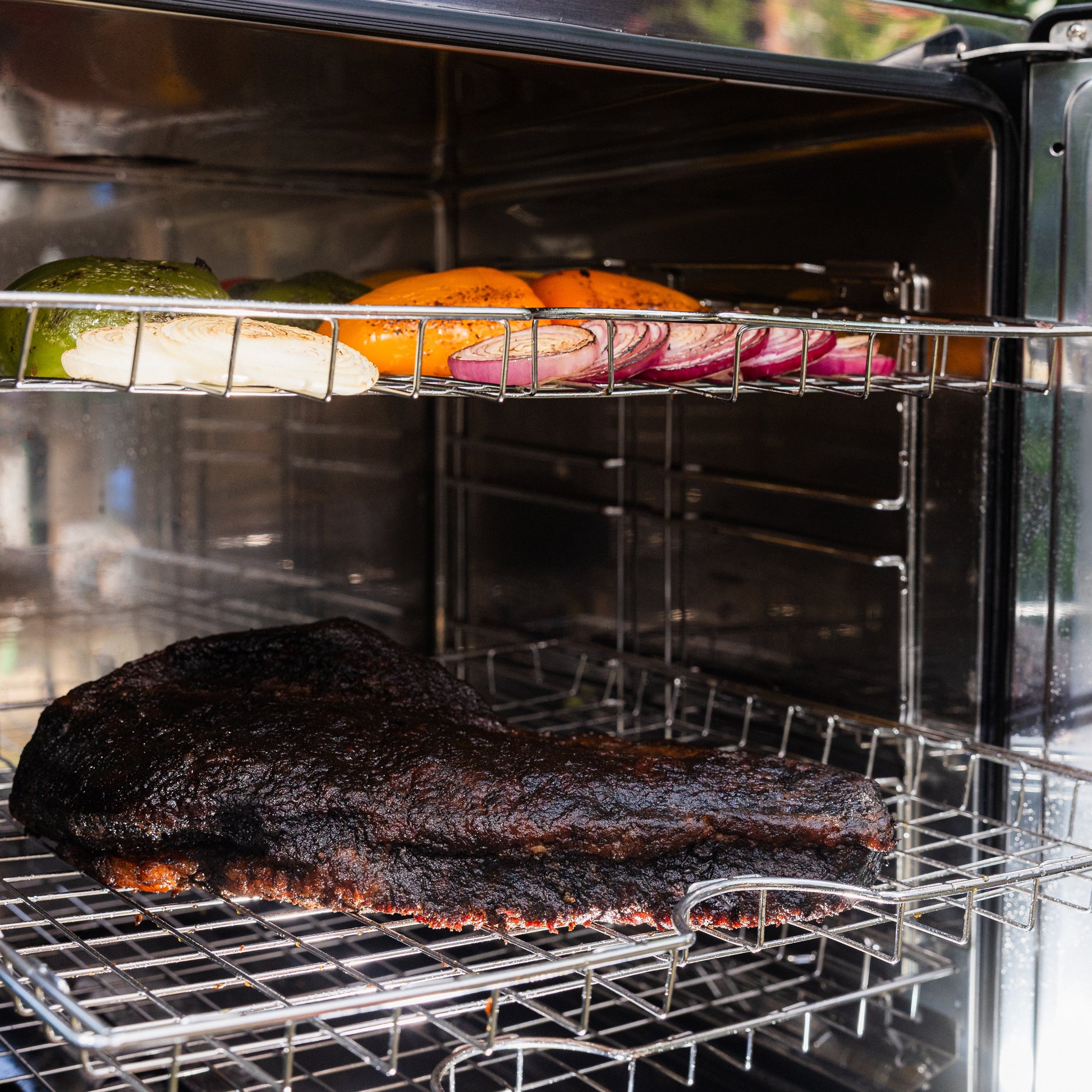 Smoked meat on a grill with vegetables inside an open smoker