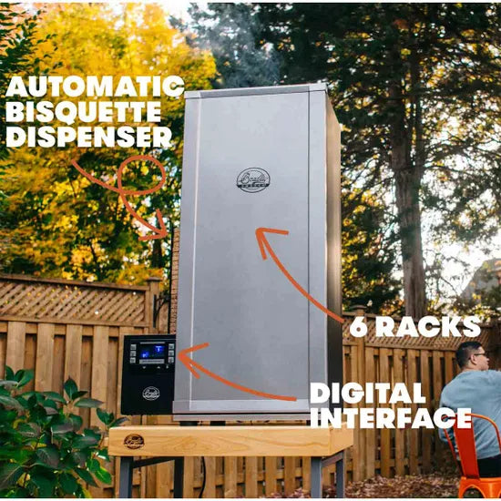 Outdoor smoker with automatic bisquette dispenser and digital interface, surrounded by trees and a wooden fence.