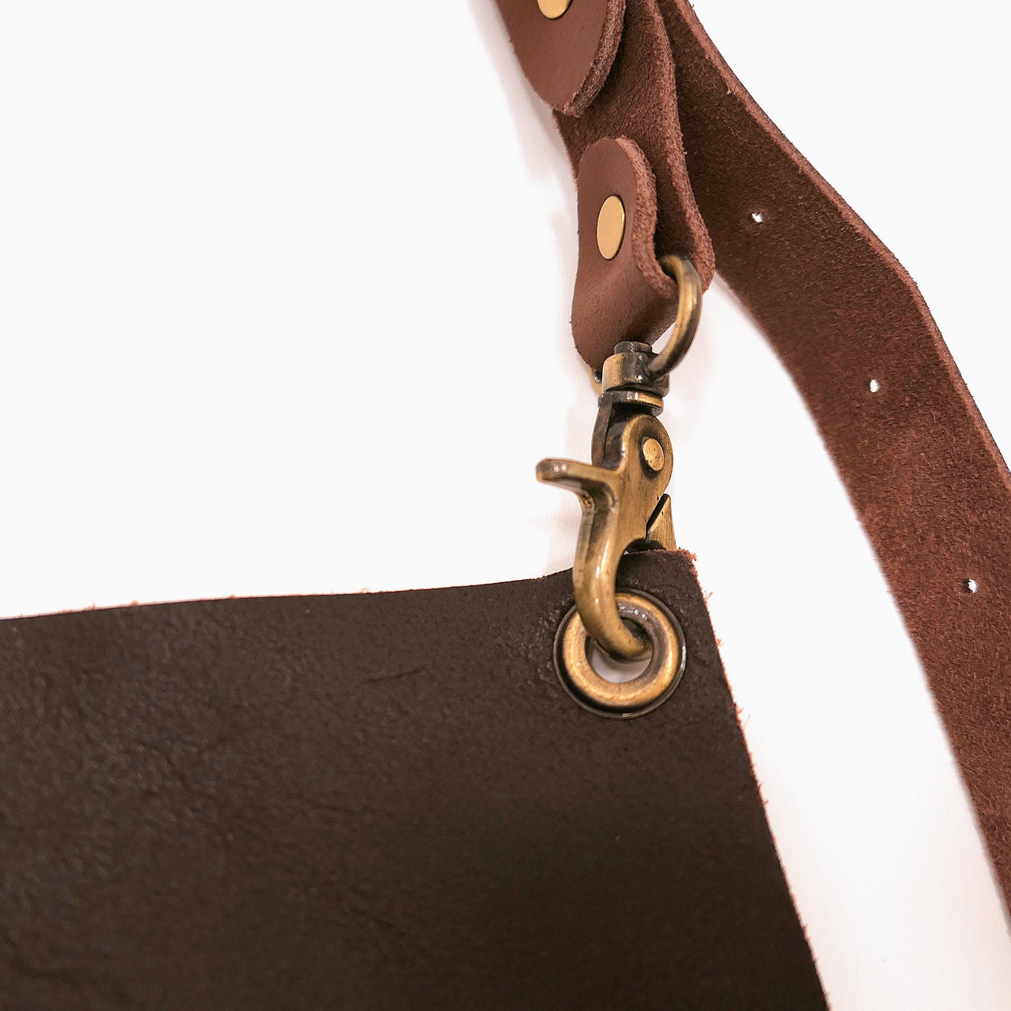 Brown leather apron with a strap and brass hook on a white background