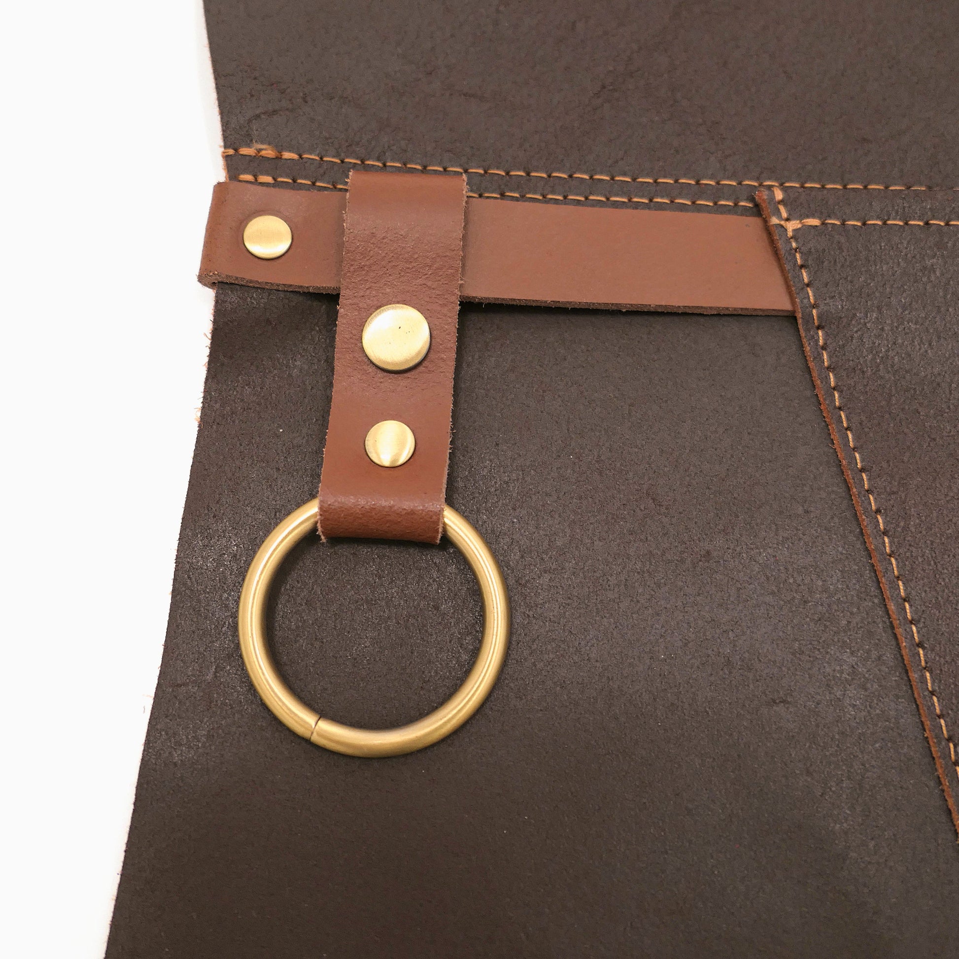 Brown leather apron with a gold ring and brass studs on a matching brown background