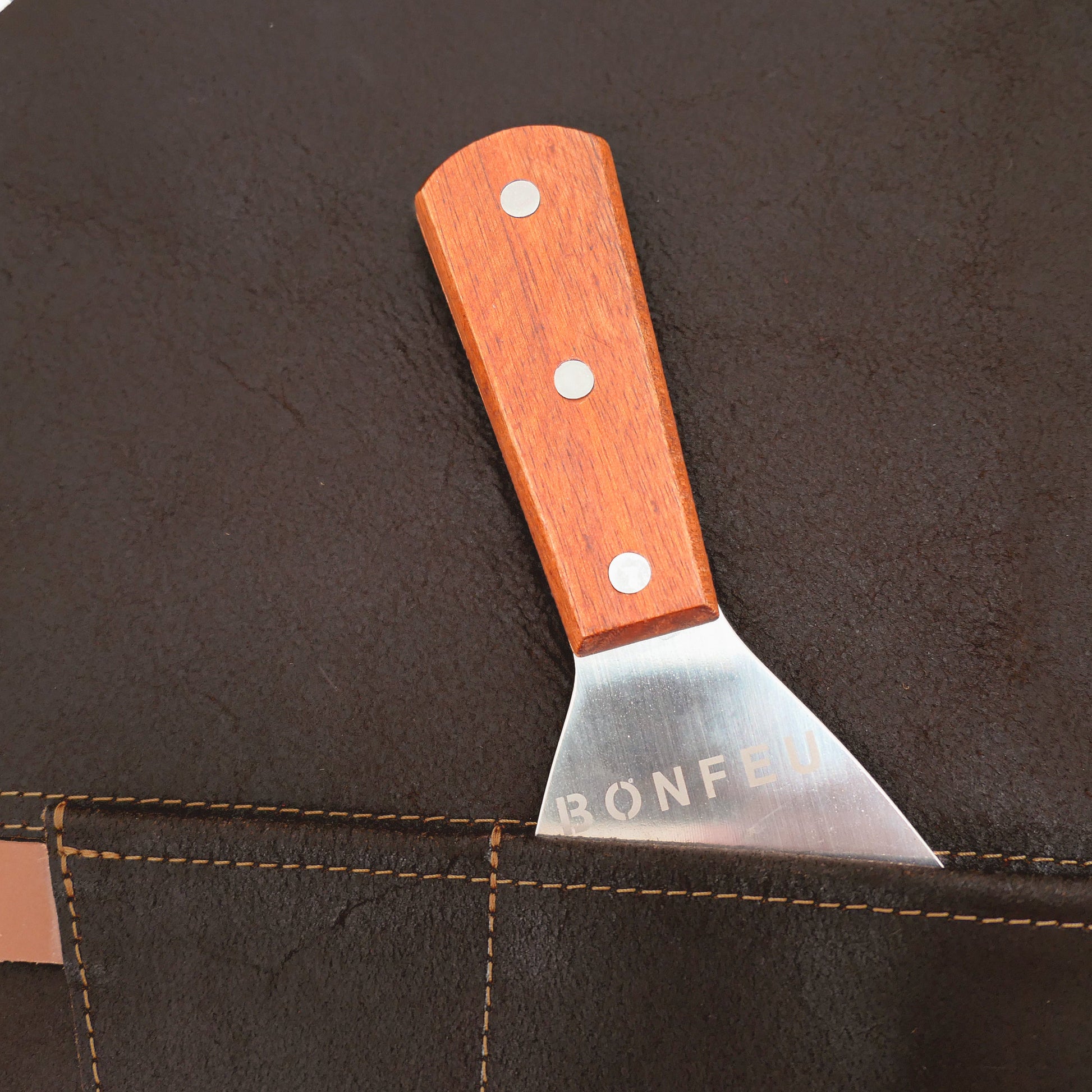 Small metal tool with wooden handle sticking out of a dark brown leather apron pocket