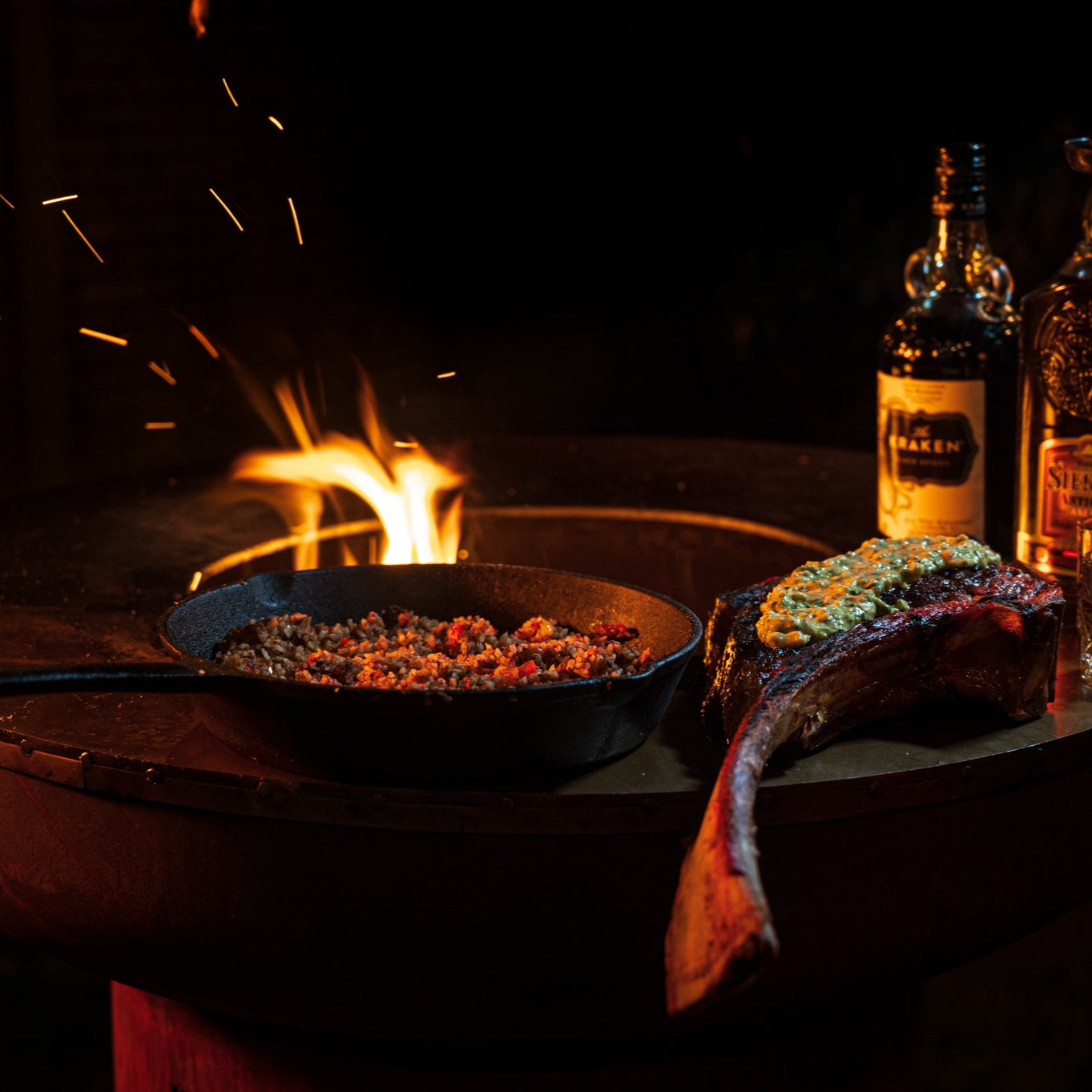 Fire pit with a skillet and two bottles of whiskey on a dark background