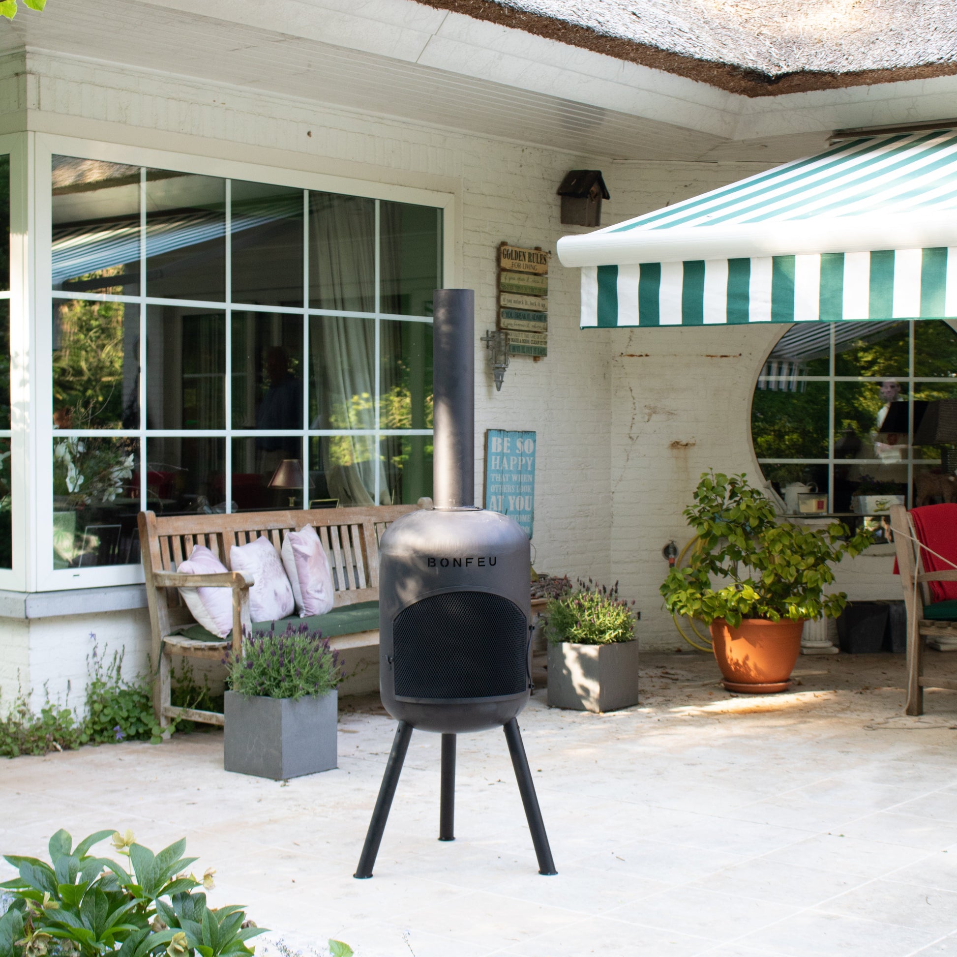Outdoor patio area with a barbecue grill, bench, and plants in front of a house.