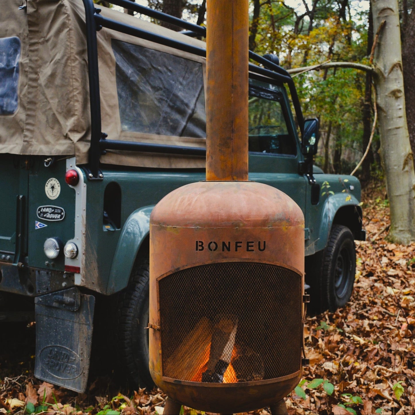 Rust-colored 'Bonfeu' fire pit in front of a green vehicle in a forest setting.