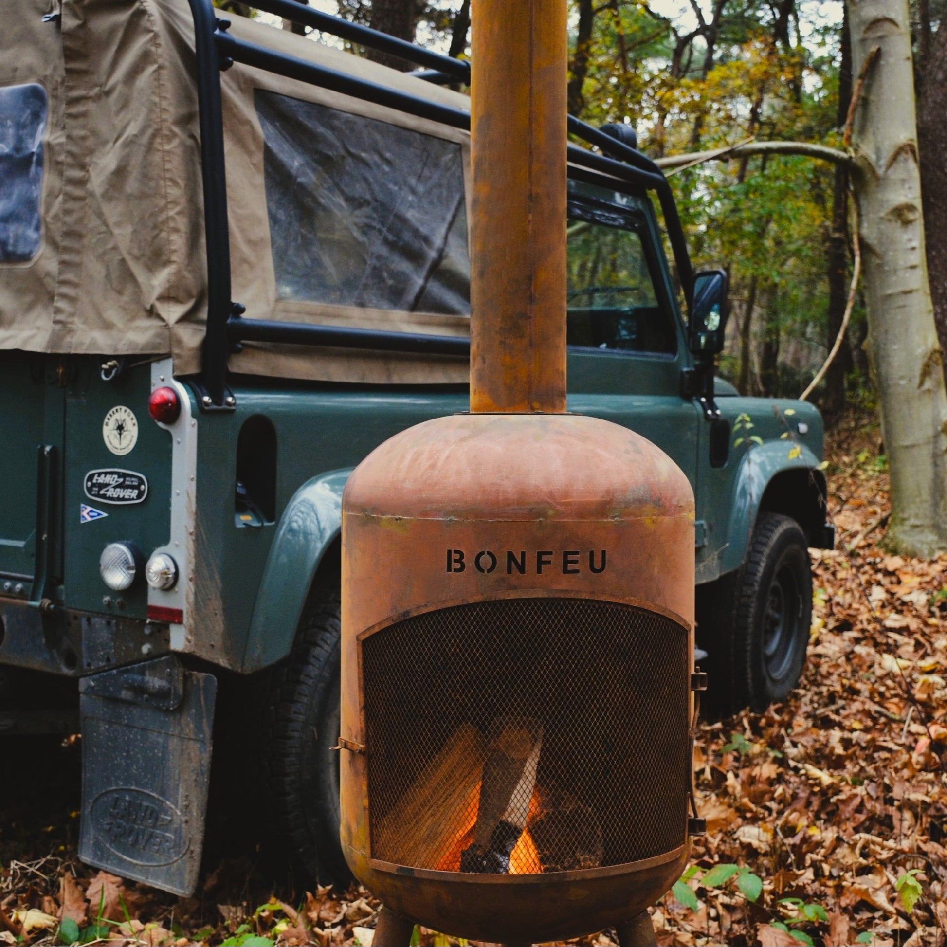 Rust-colored 'Bonfeu' fire pit in front of a green vehicle in a forest setting.