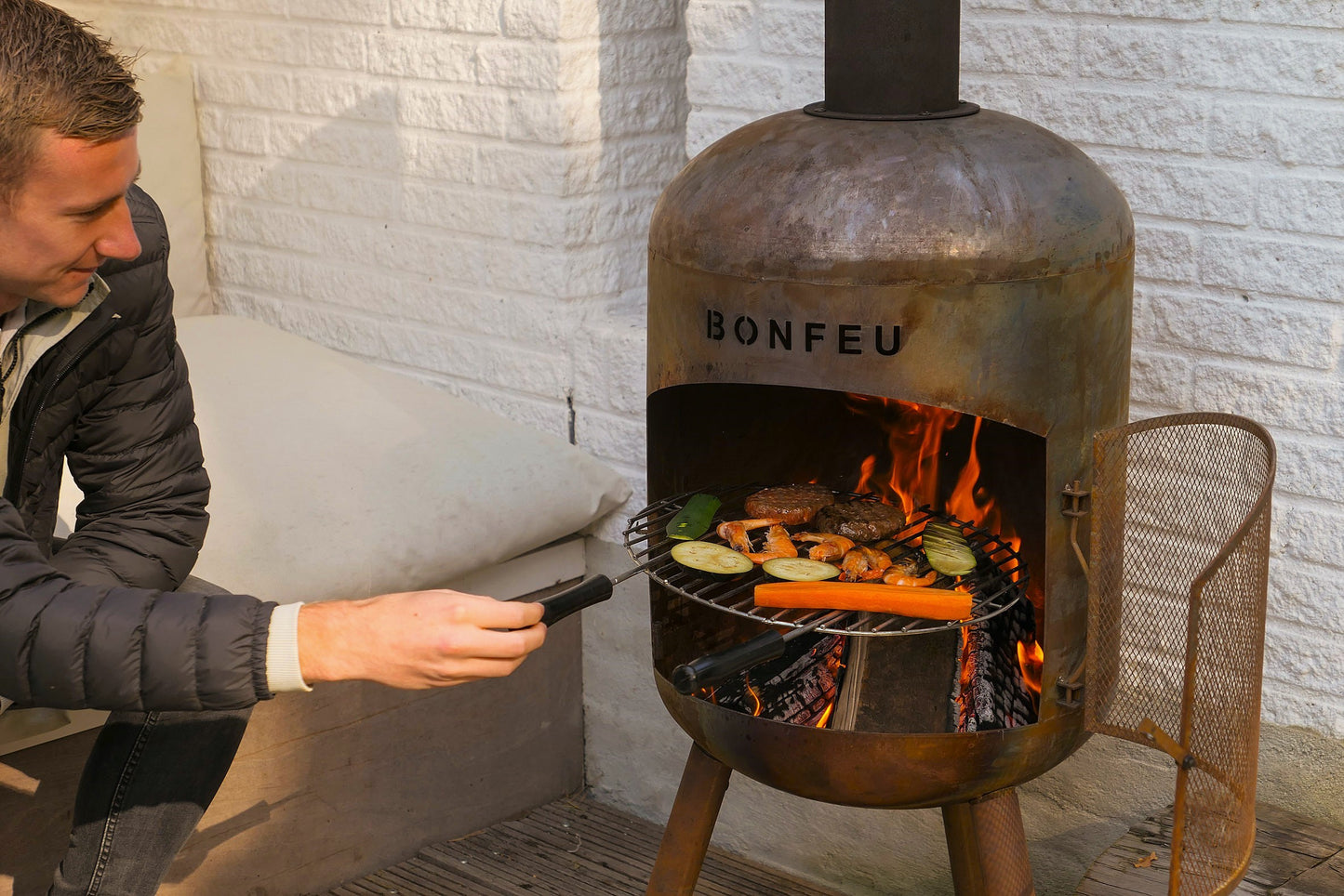 Person grilling outdoors using a Bonfeu chiminea.