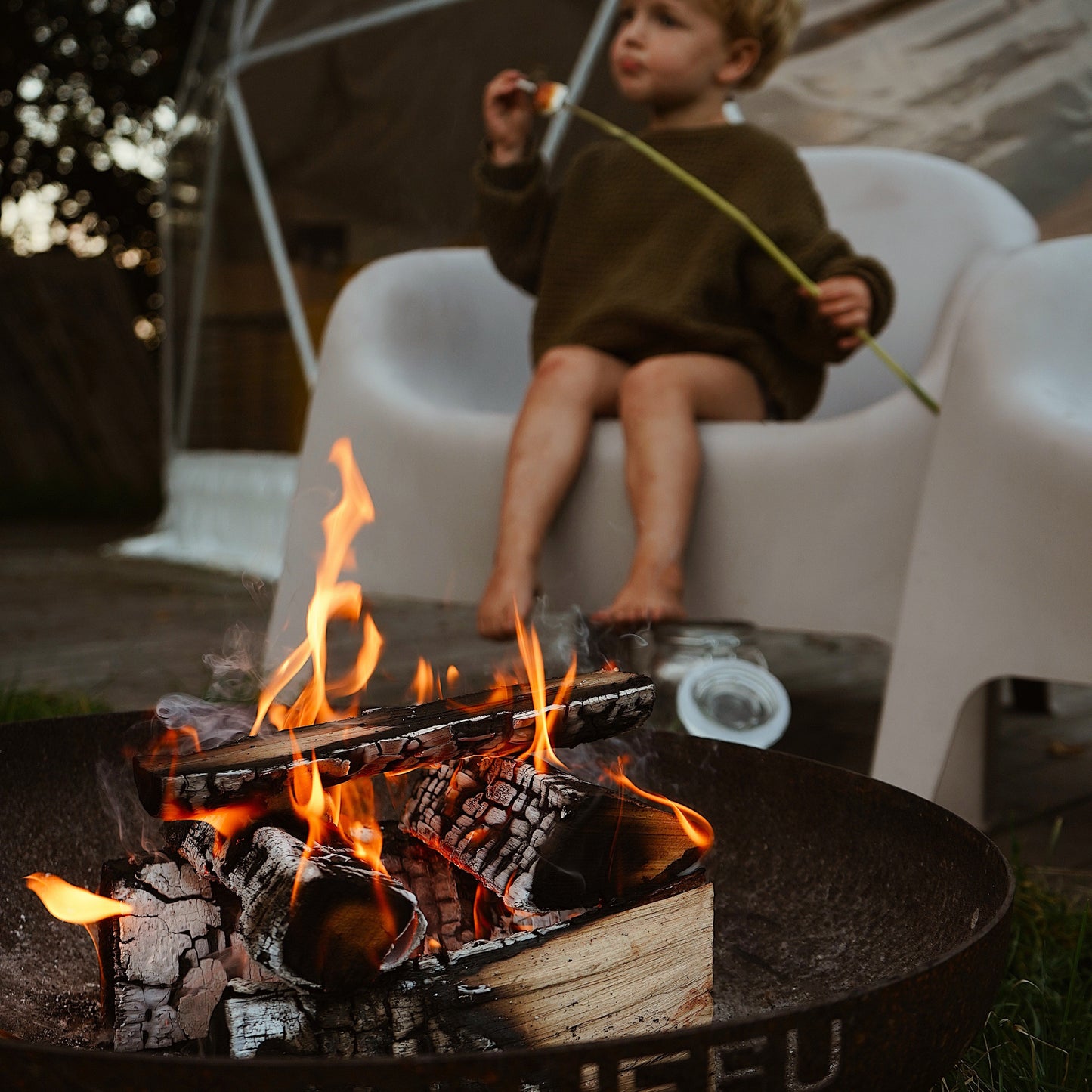 Child sitting by a fire pit with a geometric structure in the background