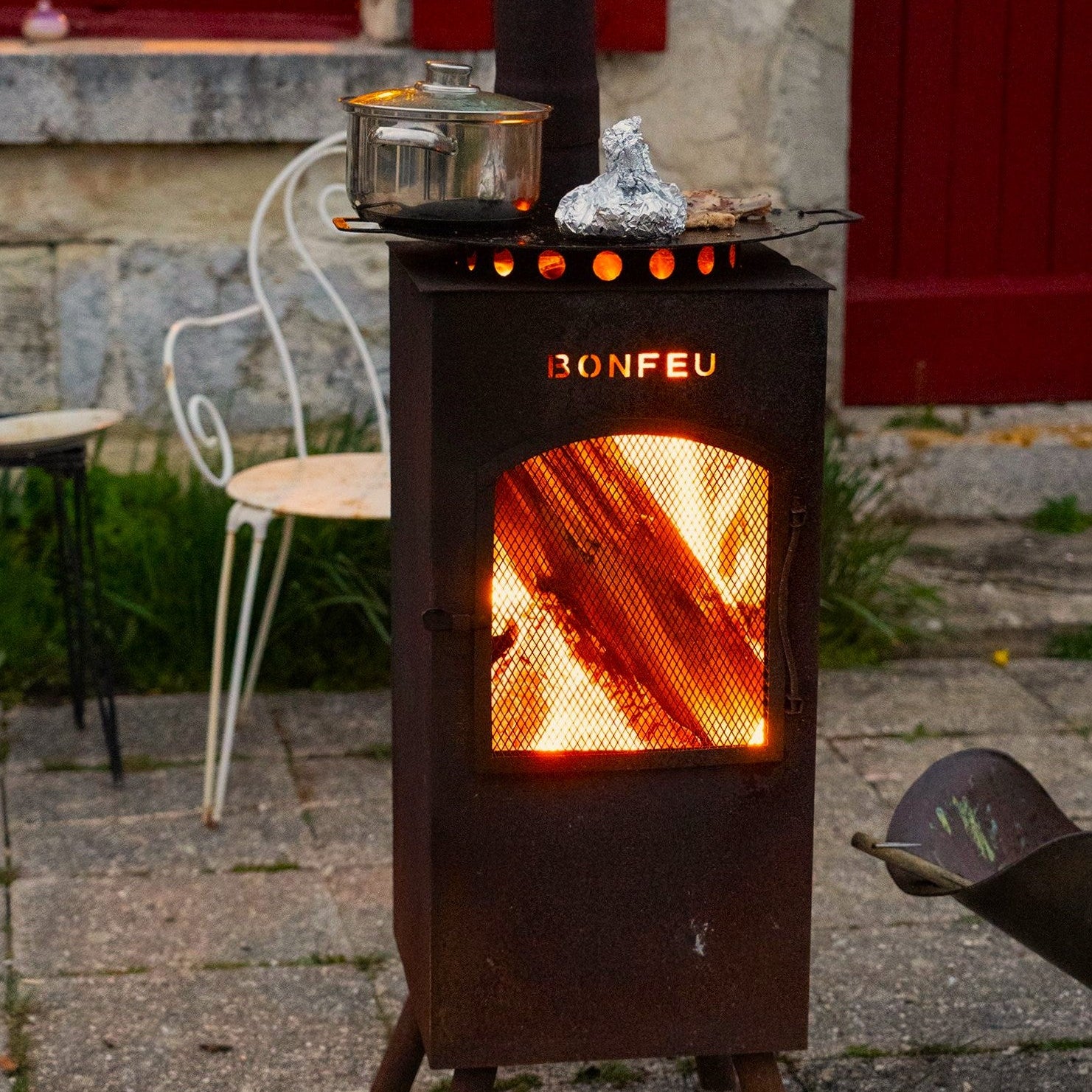 Wood-burning stove labeled 'Bonfeu' with glowing interior, outdoor setting.