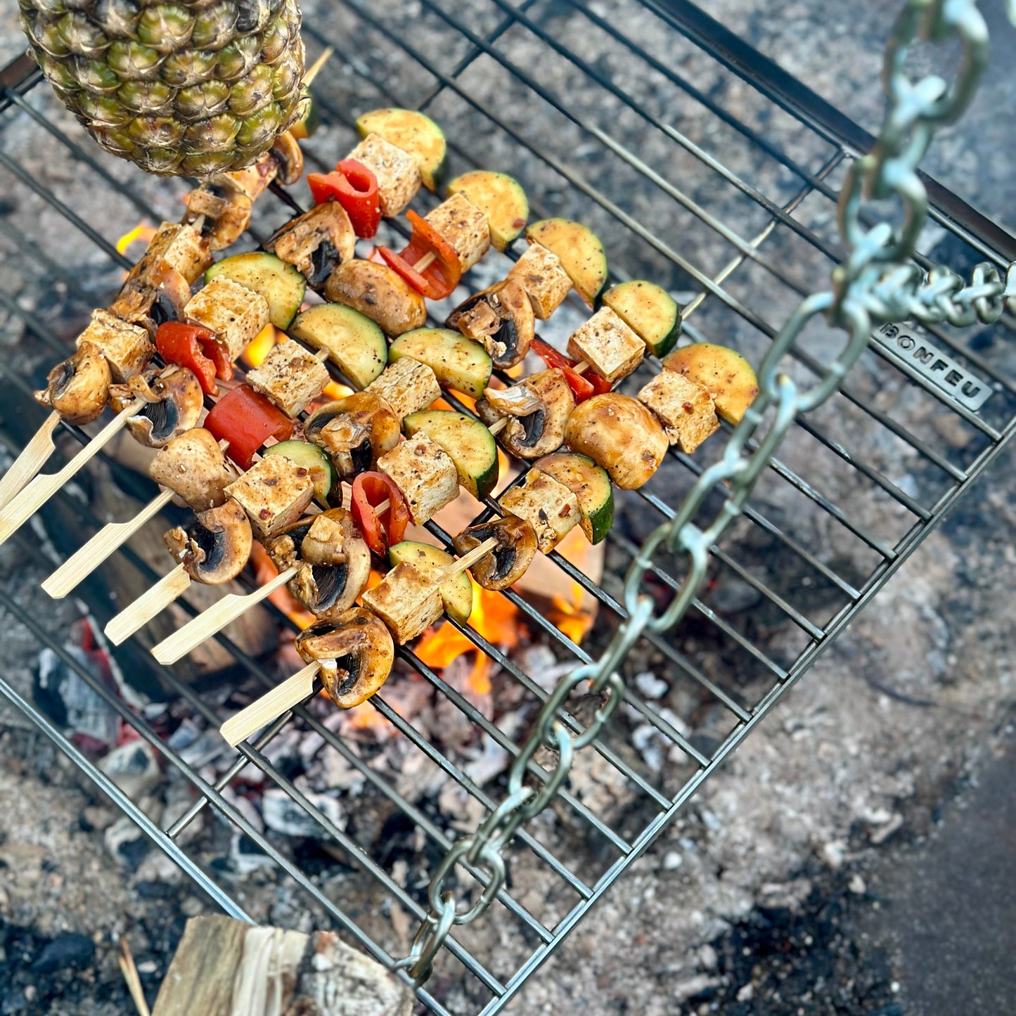 Skewers of vegetables being grilled on a metal rack over a fire.