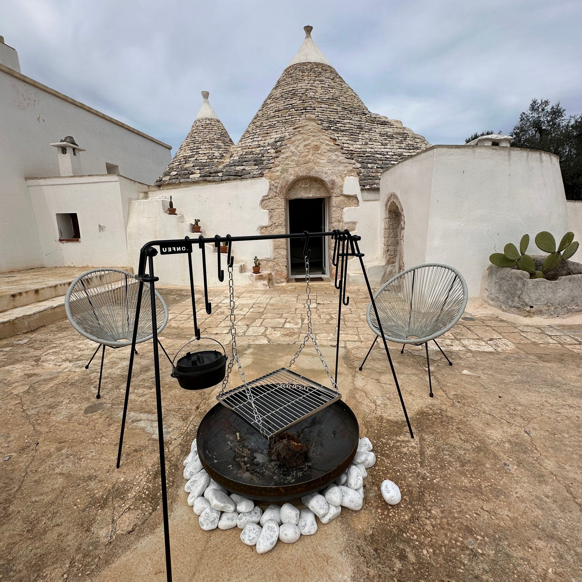 Traditional white stone building with a conical roof, outdoor seating area with chairs and a fire pit.