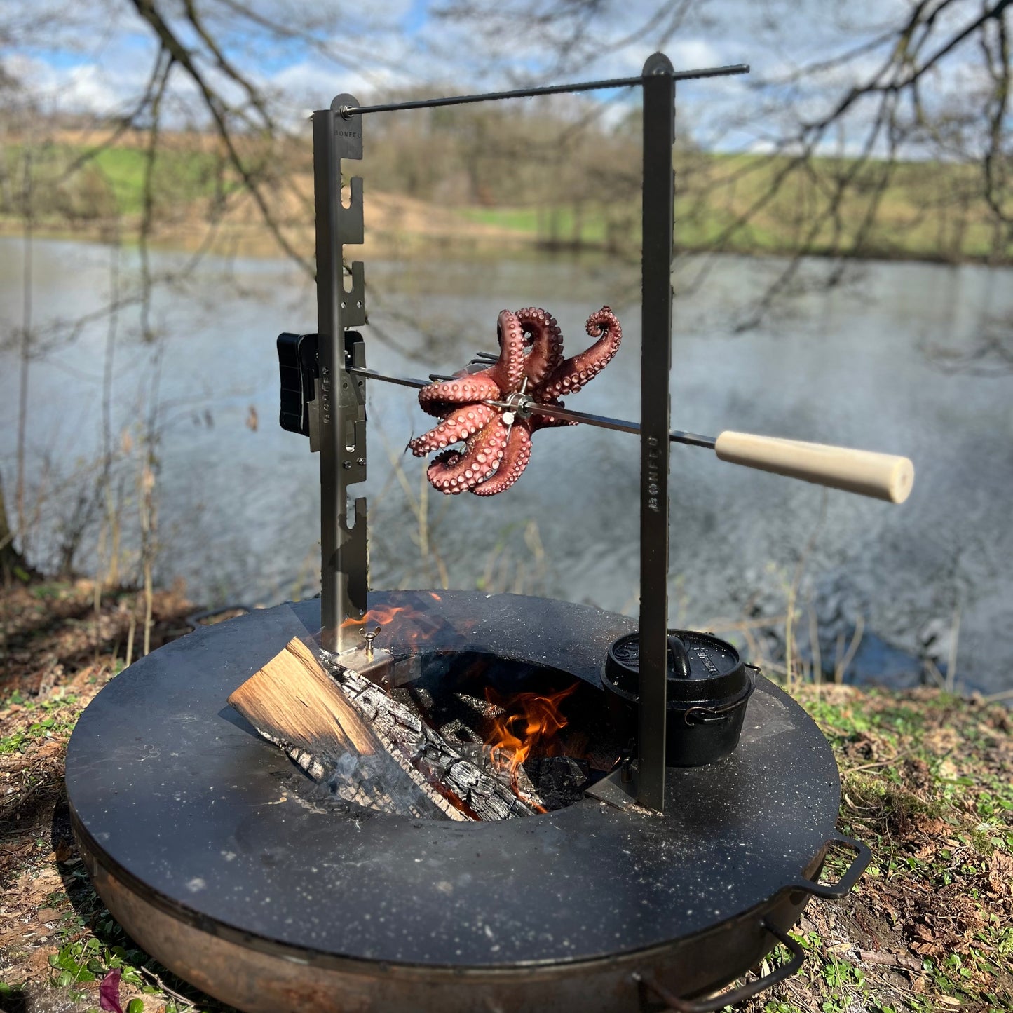 Octopus being cooked over a fire pit by a lake