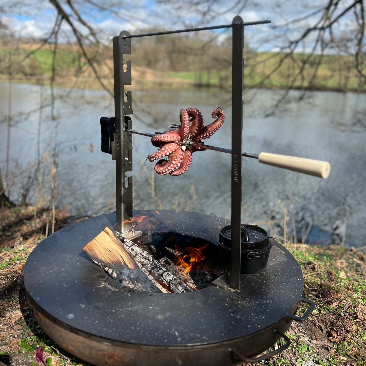 Octopus being cooked on a skewer over an open fire by a lake