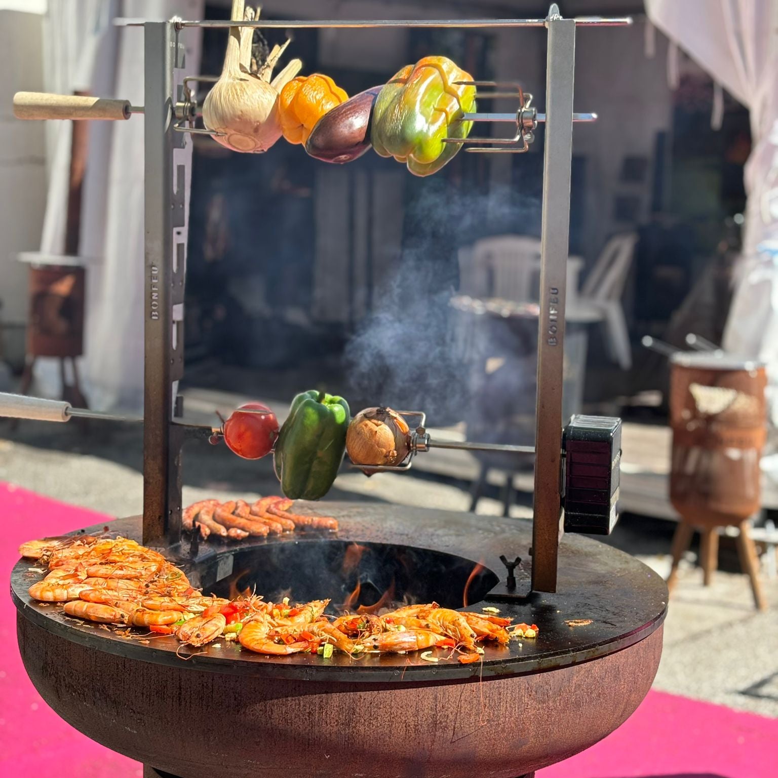 Outdoor grill with vegetables on a skewer and food cooking below, branded 'BONFEU'.