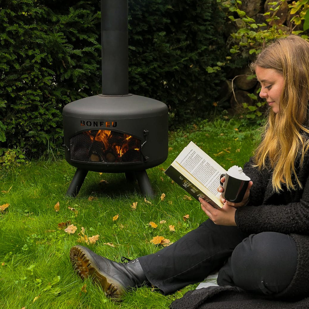 Person reading a book by a fire pit in a garden