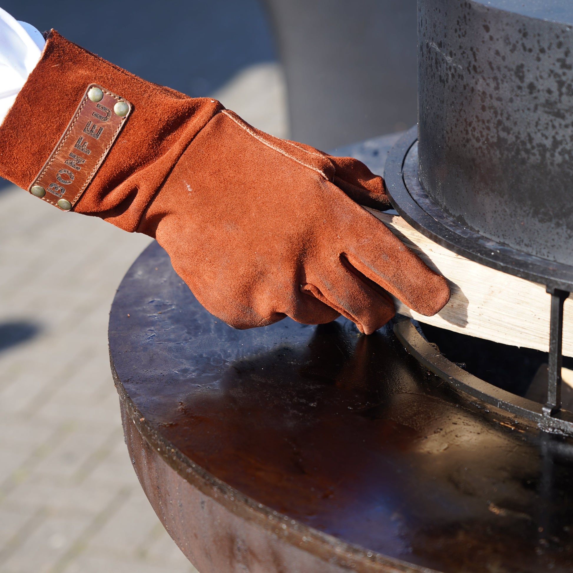 Hand wearing a brown leather glove with a metal buckle, interacting with a large metal object.