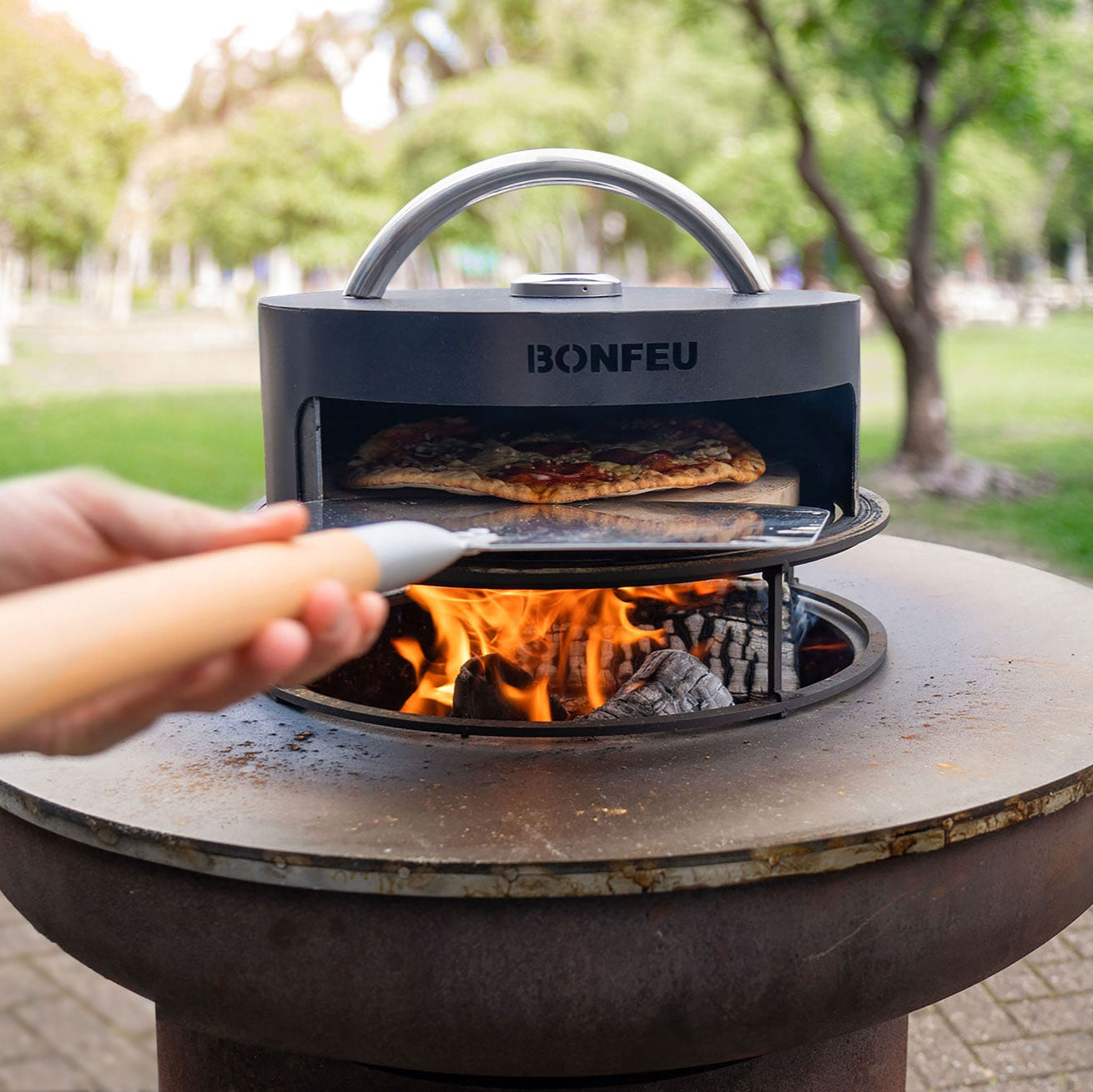 Person using a portable pizza oven labeled 'BONFEU' outdoors.