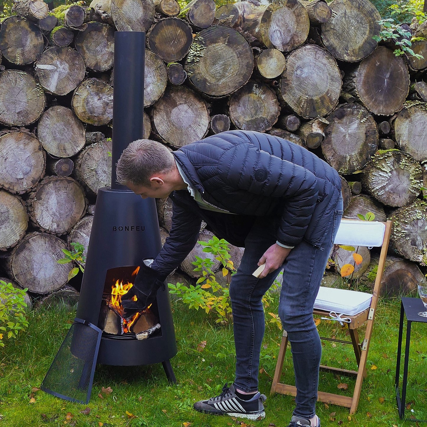 Person using a portable stove outdoors with stacked logs in the background