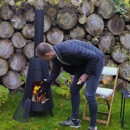 Person using a portable stove outdoors with stacked logs in the background