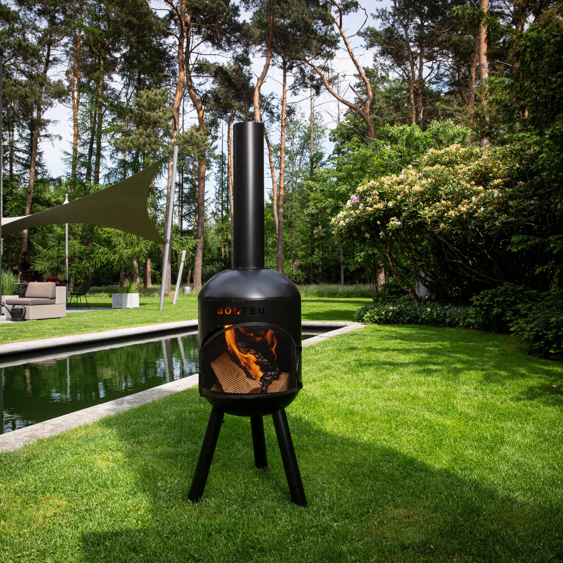 Outdoor fireplace on a grassy area with trees and a pool in the background