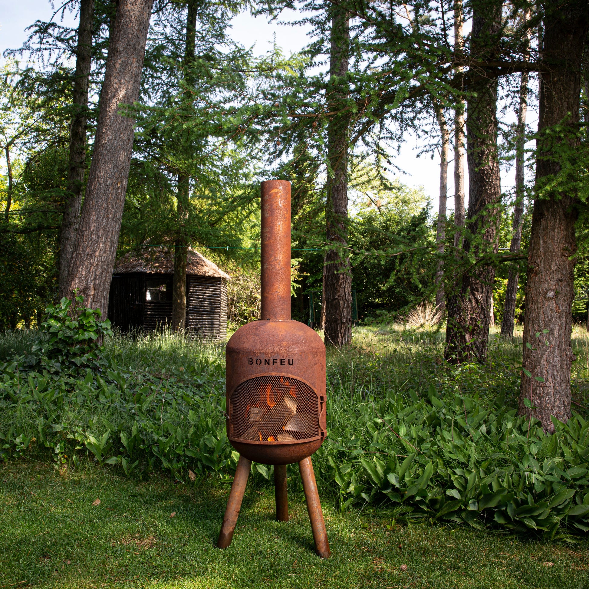 Rust-colored outdoor fireplace with 'SOMPEU' branding in a forest setting