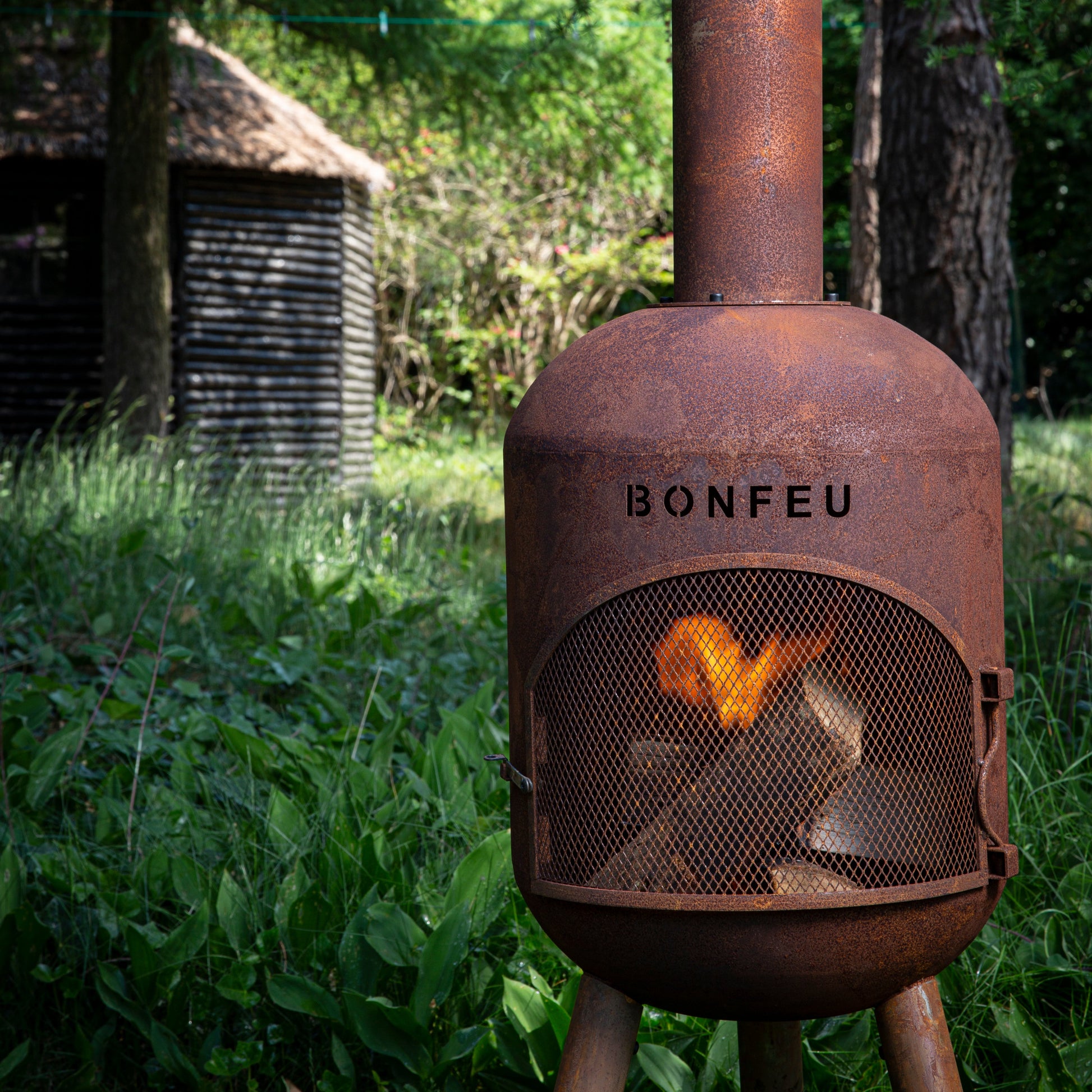 Rust-colored fire pit with 'BONFEU' branding in a forest setting