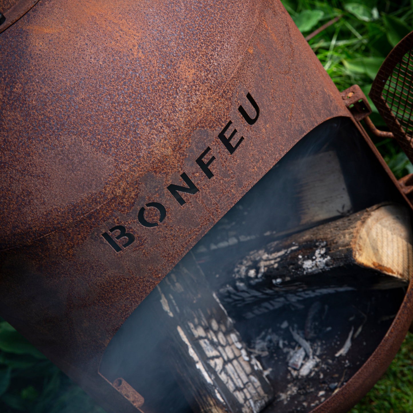 Rust-colored metal fire pit with 'BONFEU' branding on a grassy background