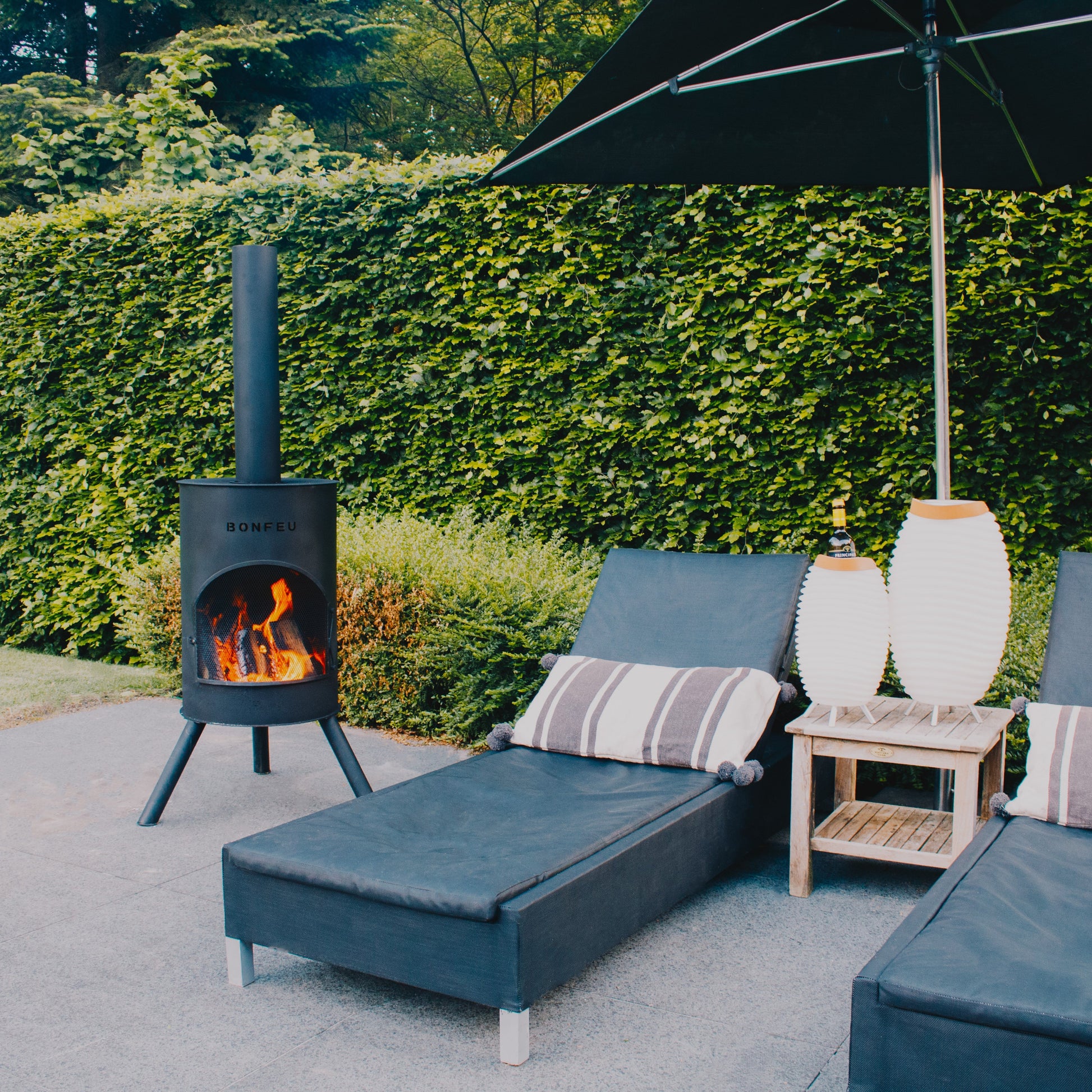Outdoor seating area with two blue lounge chairs, a small table, and a black patio heater under an umbrella.