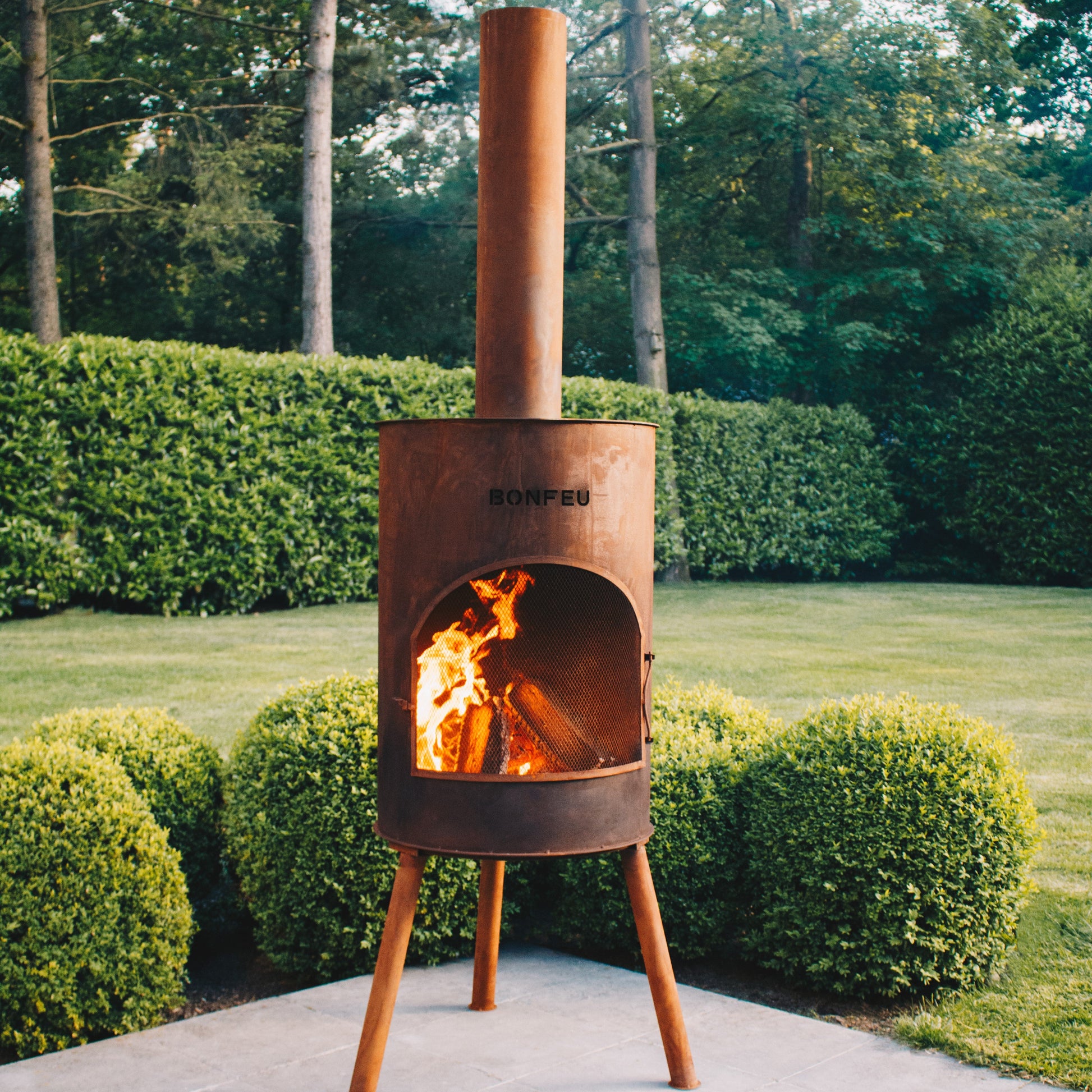 Outdoor metal fire pit with flames in a garden setting