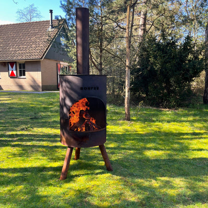 Outdoor fire pit with flames on a grassy area with trees and a building in the background
