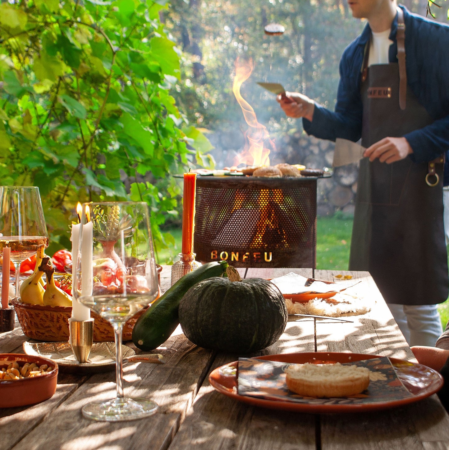 Man grilling outdoors with a table set for a meal in a garden.
