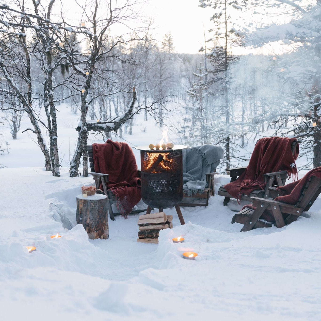 Winter scene with chairs around a fire pit in a snowy forest