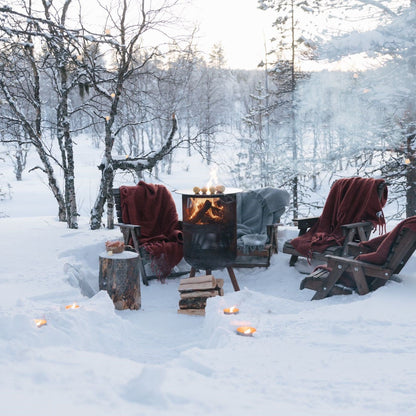 Winter scene with chairs around a fire pit in a snowy forest