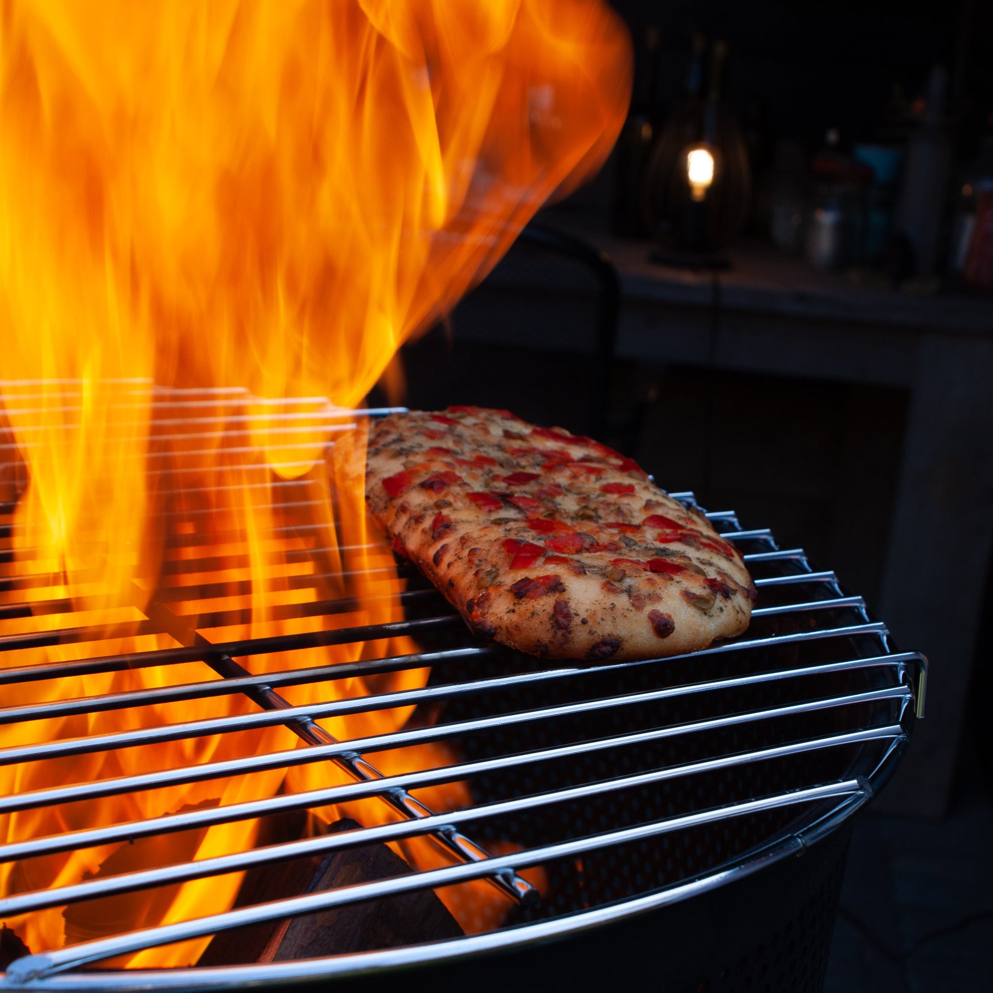 Pizza being cooked on a grill with intense flames
