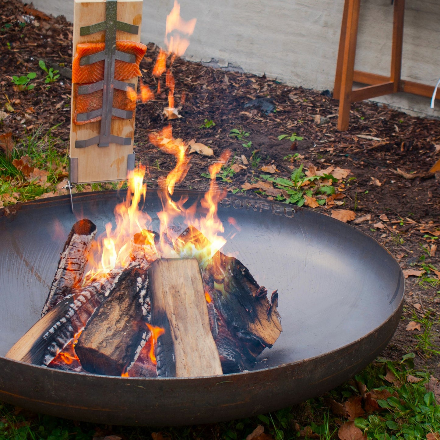 Fire pit with flames and wooden logs in an outdoor setting.