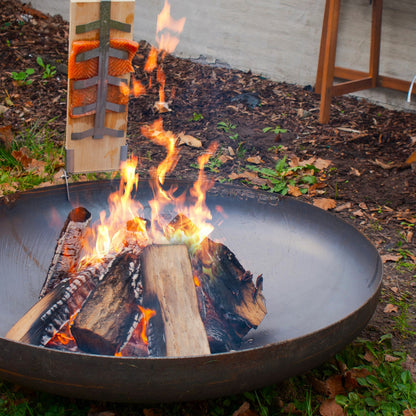 Fire pit with flames and wooden logs in an outdoor setting.