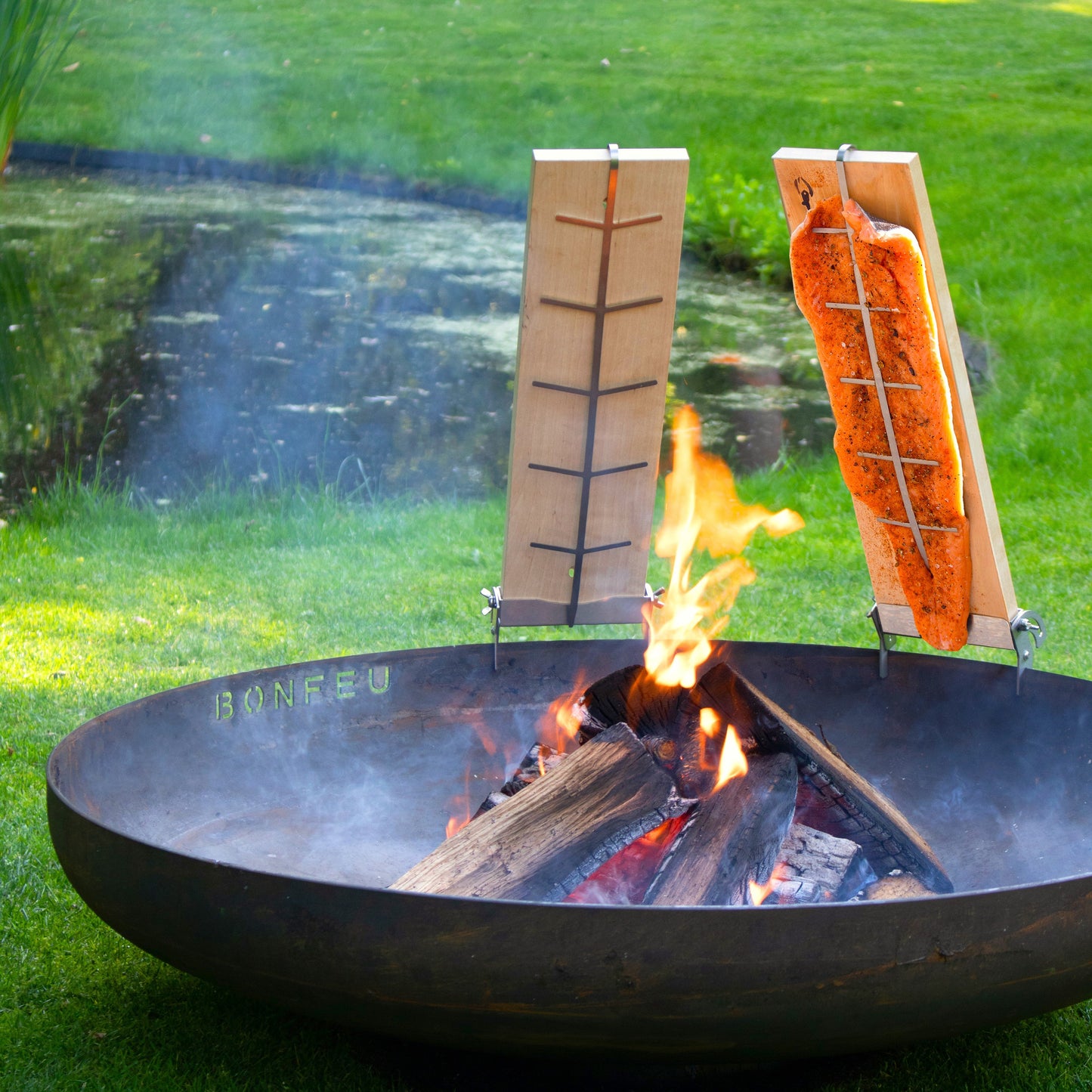 Fire pit with salmon on a wooden board over flames in a garden setting
