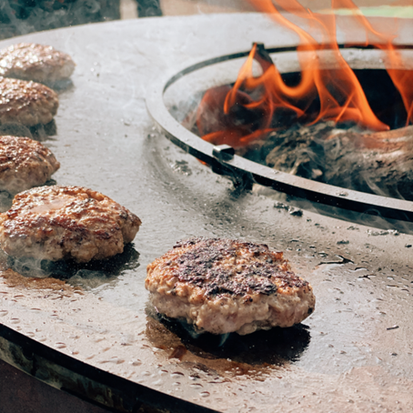 Hamburgers being cooked on a grill with flames