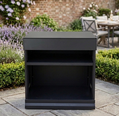 Black outdoor side table in a garden setting with flowers and a table in the background.