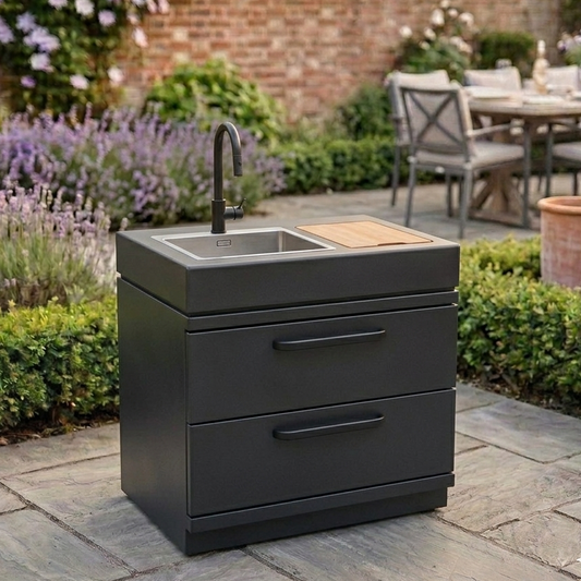 GRLLR Outdoor kitchen cabinet with sink on a patio with garden and dining area in the background