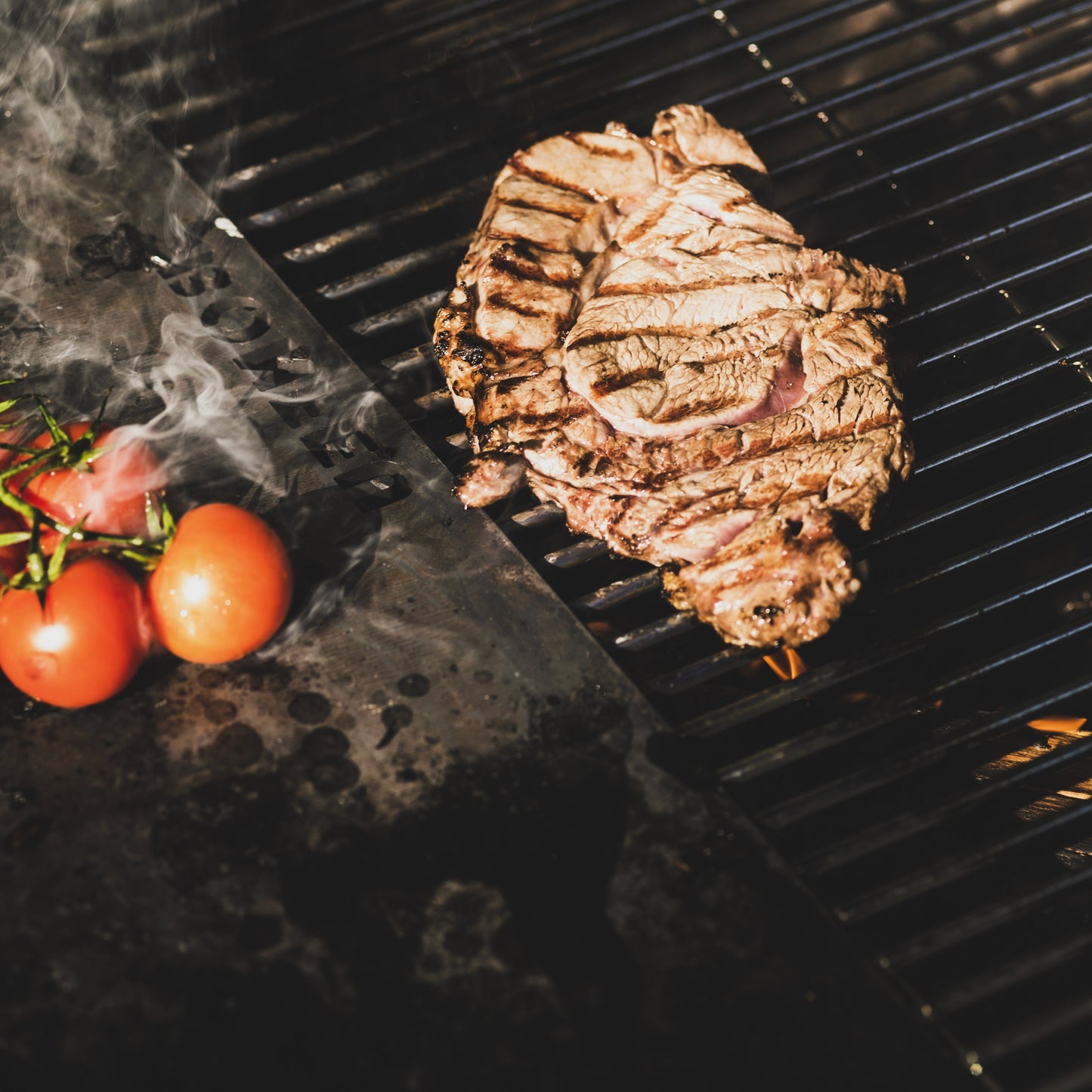 Grilled steak on a barbecue grill with cherry tomatoes nearby