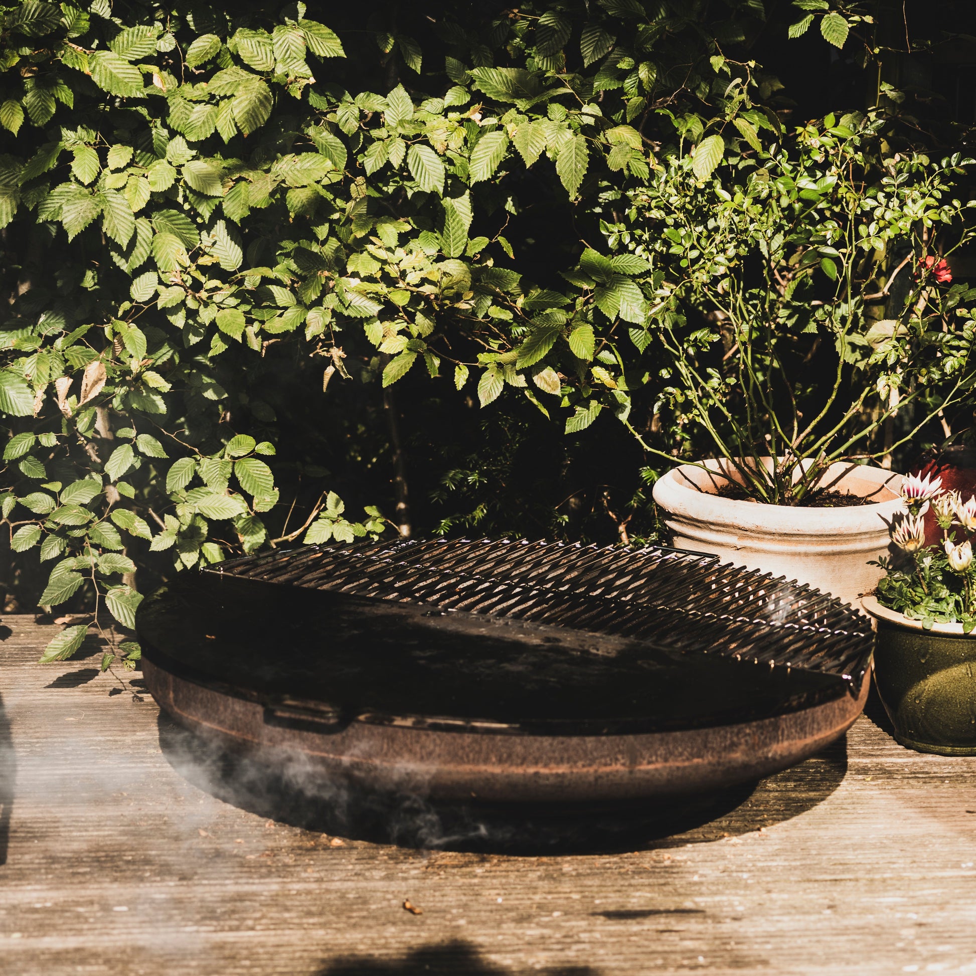 Black metal grill on a wooden deck with greenery in the background