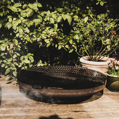 Black metal grill on a wooden deck with greenery in the background