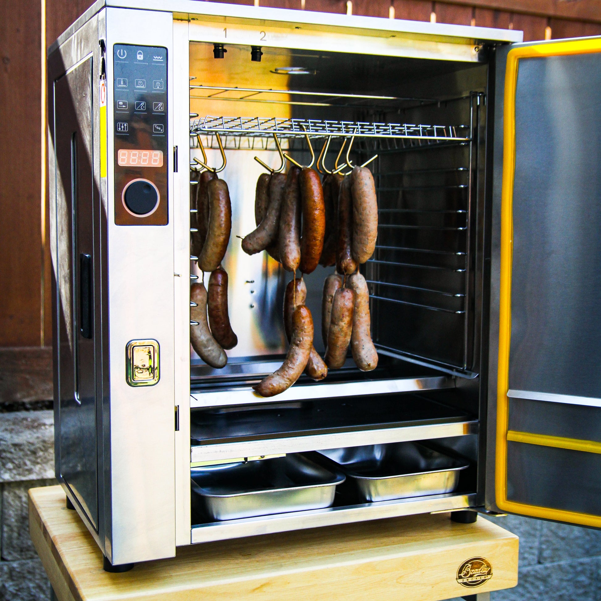Smoker grill with sausages inside, outdoors on a wooden platform.