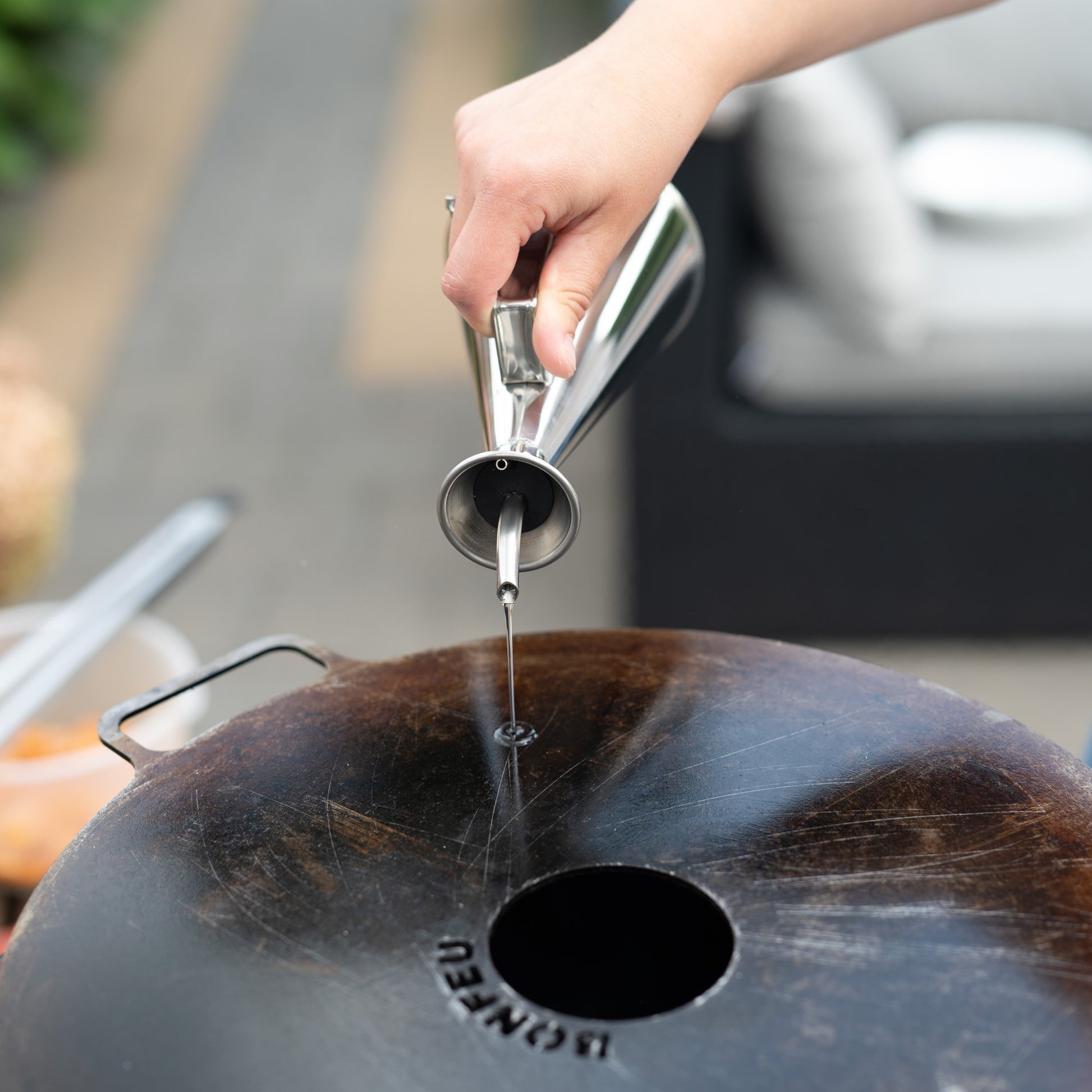 Person pouring oil into a cast iron skillet outdoors.