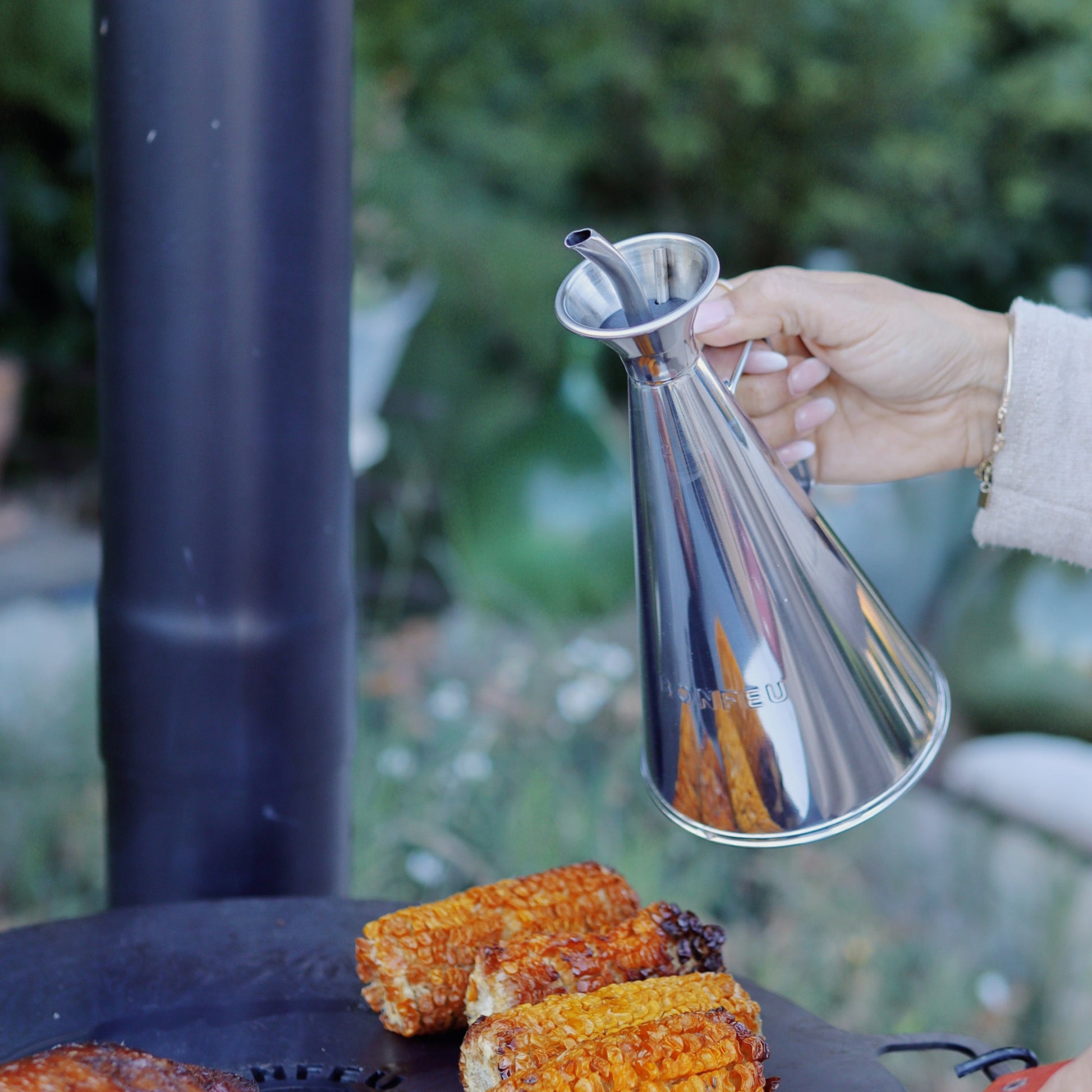 Person pouring oil over corn on a grill outdoors