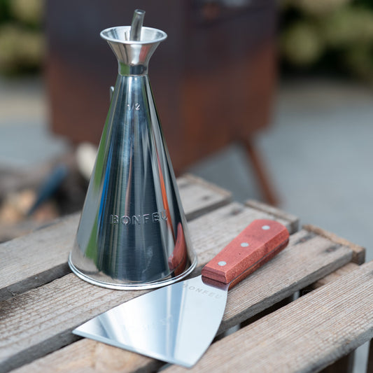 Metal olive oil dispenser and spatula on a wooden surface with a blurred background