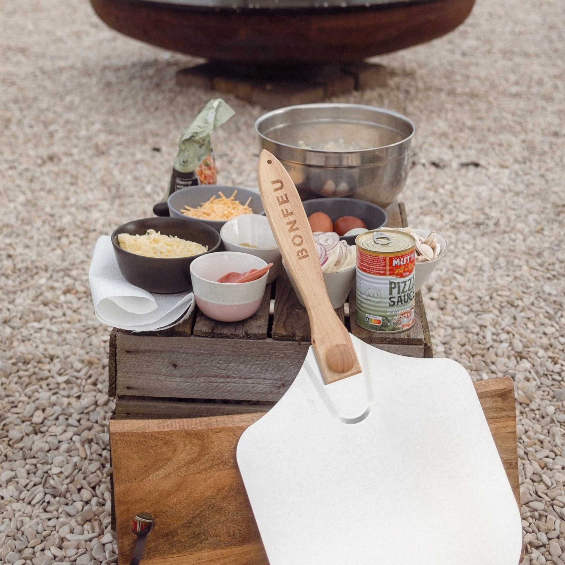 Outdoor cooking setup with a fire pit, pots, and ingredients on a wooden crate.